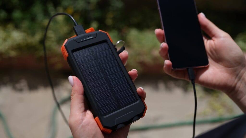 Încărcare solară în acțiune – Power bank pentru aventurieri Baterie externă solară conectată la un smartphone pentru încărcare în aer liber.
