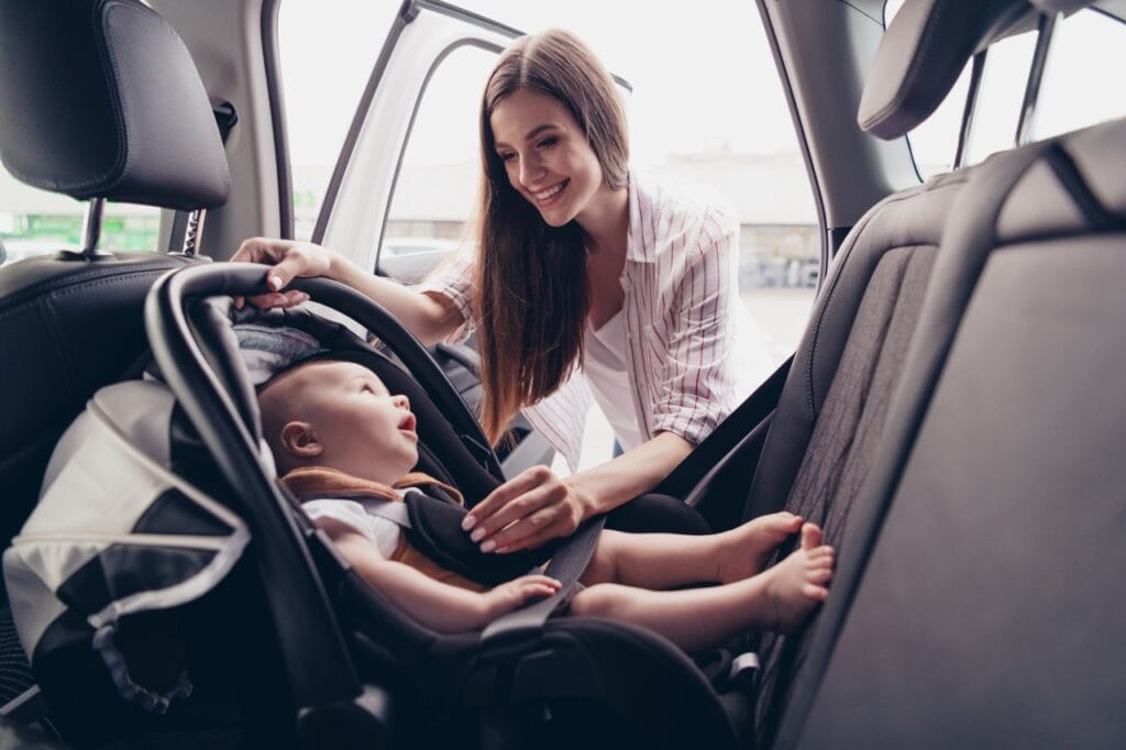 Protecția optimă a bebelușilor cu scaune auto orientate invers Mamă așază bebelușul într-un scaun auto pentru copii orientat cu spatele la direcția de mers.