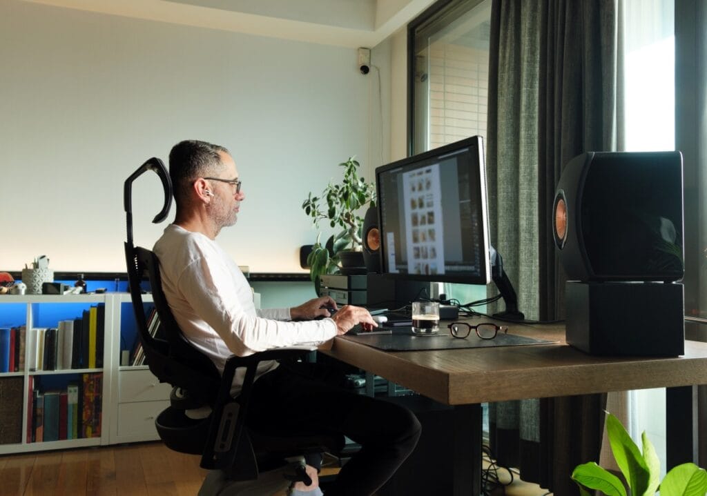 Scaunele de birou și productivitatea: De ce ergonomia contează Bărbat lucrând la birou, folosind un scaun ergonomic pentru a menține o postură corectă și a evita durerile de spate.