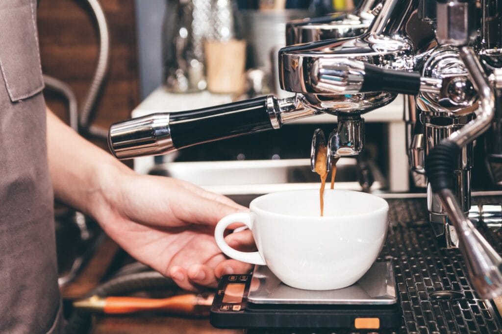 Persoană curățând un espressor profesional cu lavetă și mănuși, ghid întreținere aparat cafea.