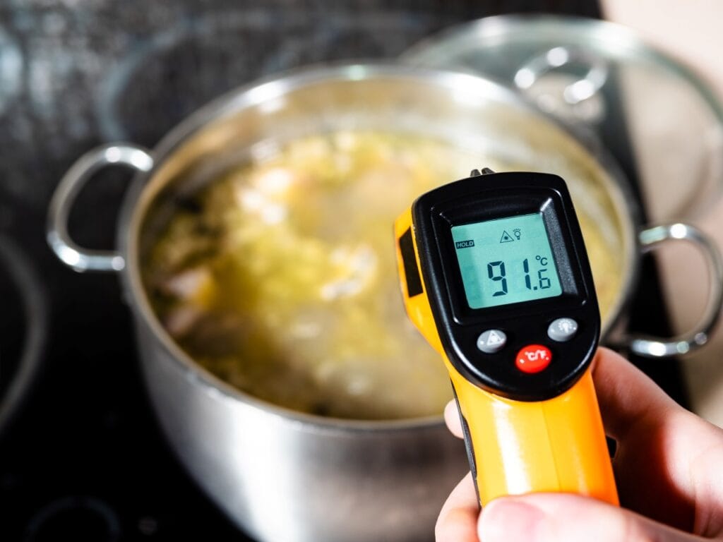 Termometru digital cu infraroșu măsurând temperatura unui lichid fierbinte într-o oală.