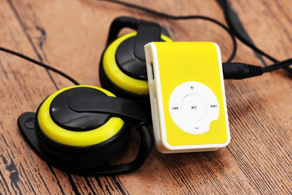 Player MP3 cu design compact și autonomie extinsă MP3 player galben cu butoane de control și căști retro negre cu galben, pe fundal de lemn – dispozitiv audio portabil cu autonomie mare