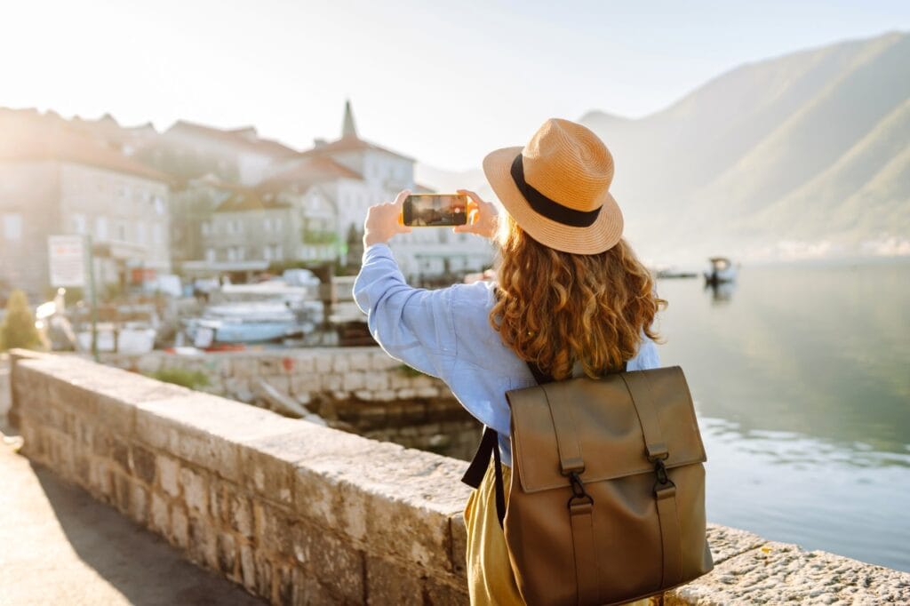 Zoom periscopic: tehnologia care schimbă modul în care fotografiem Femeie fotografiind cu telefon cu cameră periscopică un oraș turistic de pe malul apei