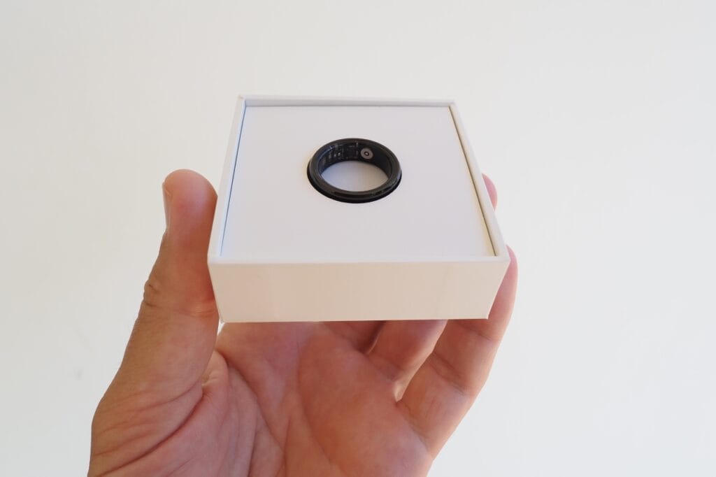 Inel inteligent prezentat elegant într-o cutie minimalistă Inel inteligent negru în cutie albă minimalistă, ținut în mână, simbolizând tehnologia purtabilă și compatibilitatea cu smartphone-uri Android și iOS