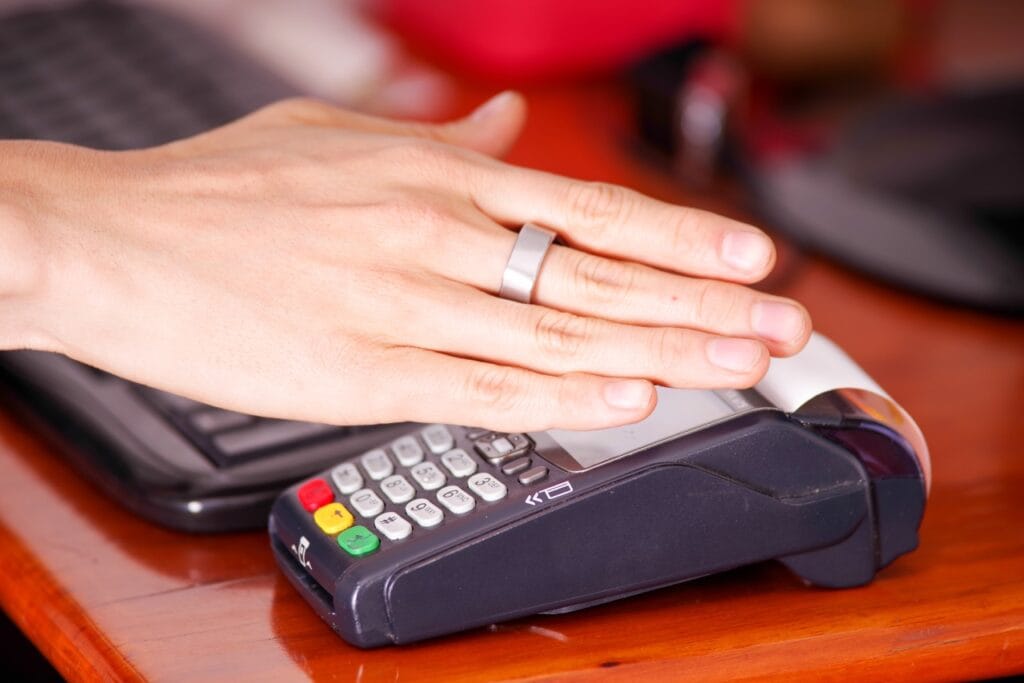 Plăți inteligente și sigure cu un simplu gest – inelul digital Mână cu inel inteligent care efectuează o plată contactless la un terminal POS, tehnologie NFC sigură pentru plăți digitale.