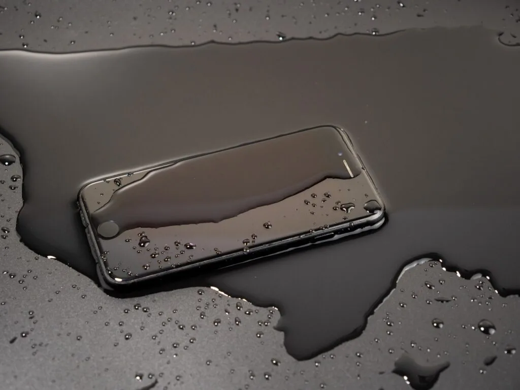 Ce trebuie să știi despre folie și impermeabilitatea telefonului tău Telefon smartphone ud pe o suprafață neagră, expus la apă