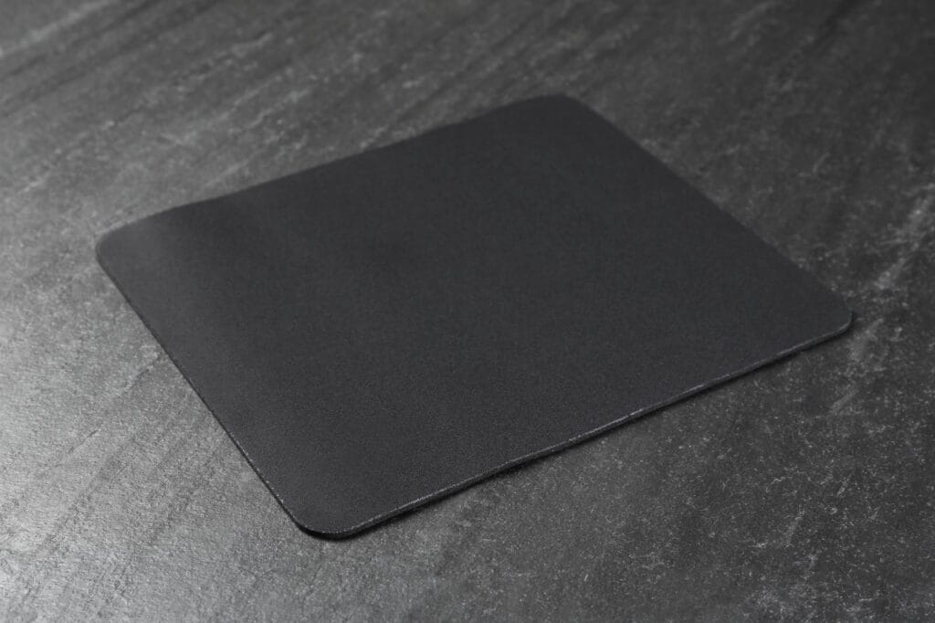 Grosimea mousepad-ului și impactul asupra performanței în gaming Mousepad negru subțire așezat pe un birou din material dur – ideal pentru gaming de precizie