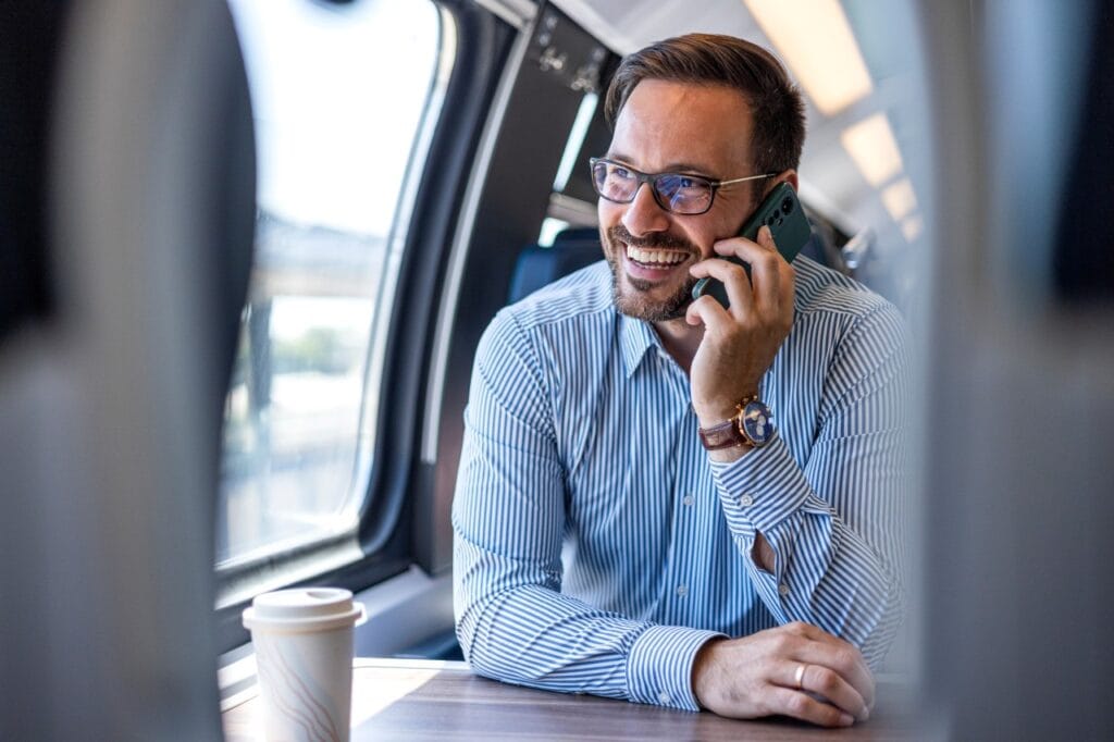 Design premium, performanță de top: cum contează materialele în alegerea unui flagship Bărbat vorbind la telefon mobil într-un tren modern, purtând cămașă și ceas, reprezentând utilizarea unui smartphone premium în deplasare