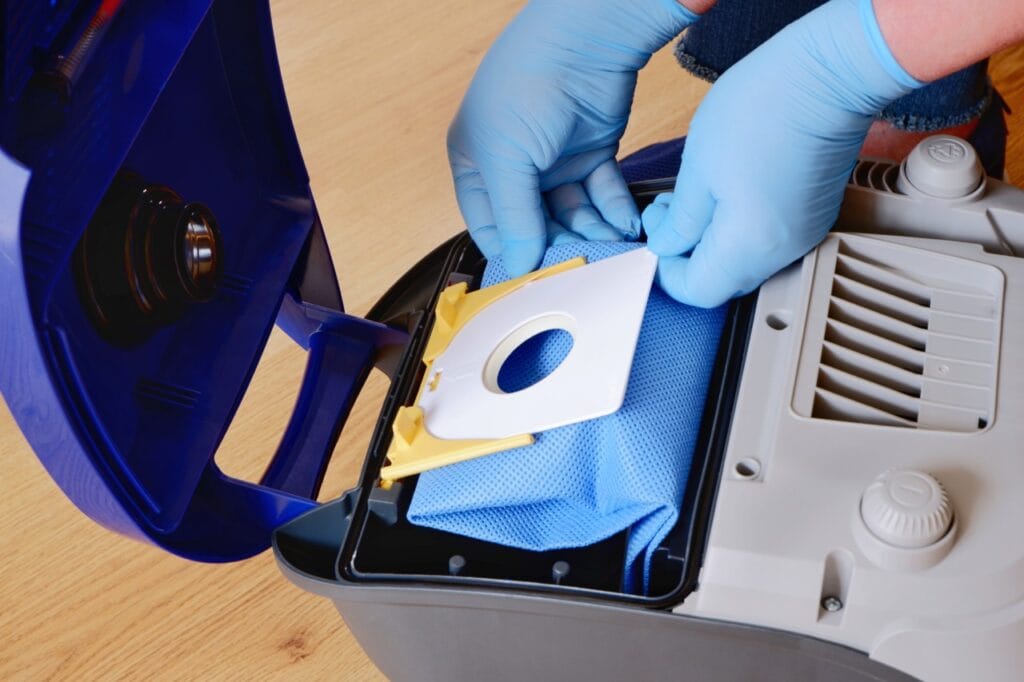 Cum prelungești viața aspiratorului tău cu sac Persoană echipată cu mănuși schimbând sacul unui aspirator, demonstrând întreținerea corectă a electrocasnicului.