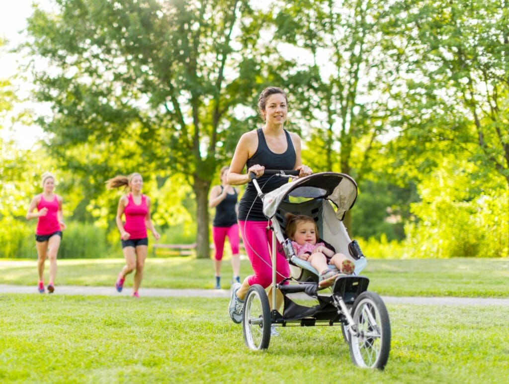 Căruciorul sport potrivit vârstei copilului – siguranță și confort la fiecare etapă Femeie alergând cu un cărucior sport pentru copil mic într-un parc, evidențiind un model potrivit pentru vârste peste 6 luni.