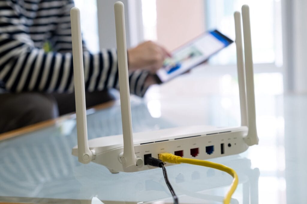 Router wireless cu patru antene și conexiune prin cablu LAN, amplasat pe masă din sticlă pentru semnal Wi-Fi optim în casă.