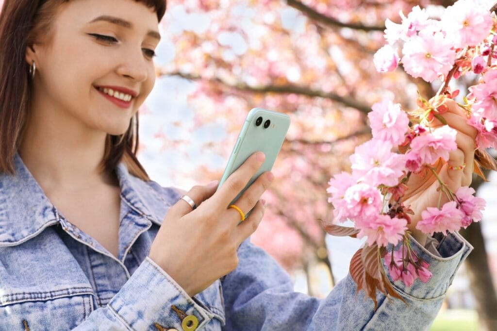 Când să folosești modul Auto și când pe cel Pro pe telefonul tău Tânără făcând poză florilor de cireș cu telefonul în modul Auto, fotografie rapidă de primăvară