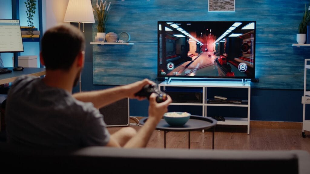 Gaming de calitate: importanța rezoluției și a ratei de refresh Persoană jucând un joc video pe consolă la televizor 4K cu rată de refresh mare, într-un living modern