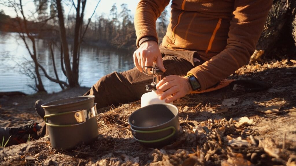 Camping de nouă generație: cum alegi un arzător cu tehnologie eficientă Arzător camping portabil high-tech folosit în apropierea unui lac de către excursionist