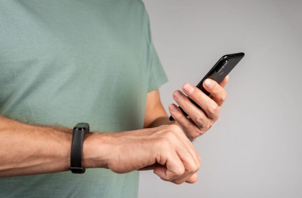 Compatibilitatea între brățările fitness și smartphone-ul tău: Android vs iOS Bărbat sincronizând brățara fitness cu smartphone Android, concept compatibilitate dispozitive fitness iOS vs Android