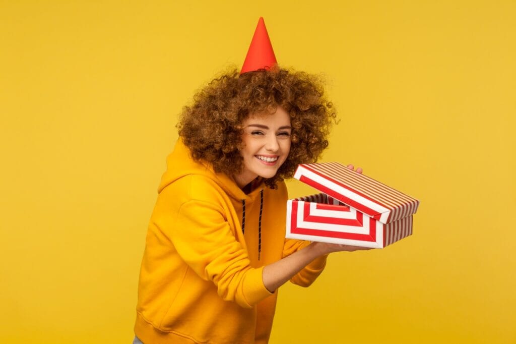 Femeie tânără zâmbitoare cu un cadou deschis în mână, purtând o pălărie de petrecere – cadou last-minute livrat rapid