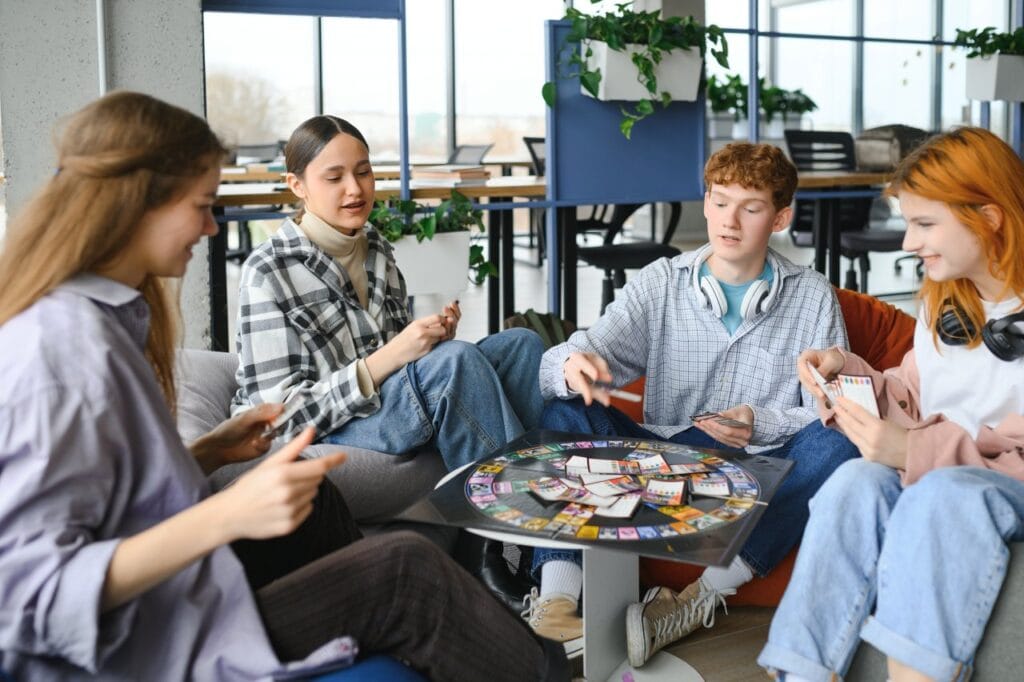 „Strategie, cunoștințe și multă distracție” Tineri adolescenți jucând un joc de societate educativ într-un spațiu de socializare modern.