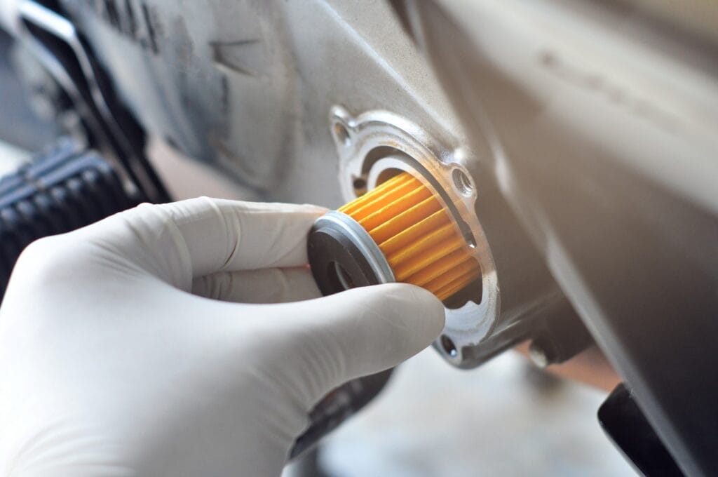 Mână cu mănușă verificând supapa unui filtru de ulei auto, importantă pentru funcționarea optimă a motorului