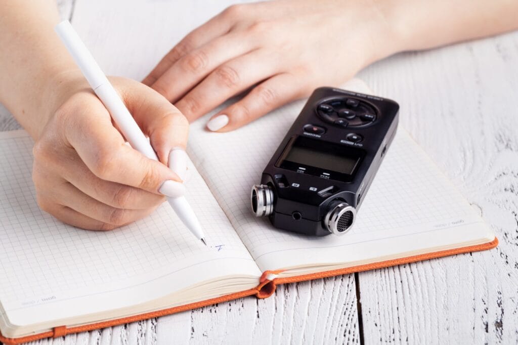 Autonomia bateriei la reportofoane: cât de importantă este pentru înregistrări fără griji Înregistrare audio și notițe scrise manual – imagine care sugerează necesitatea unui reportofon cu baterie de durată