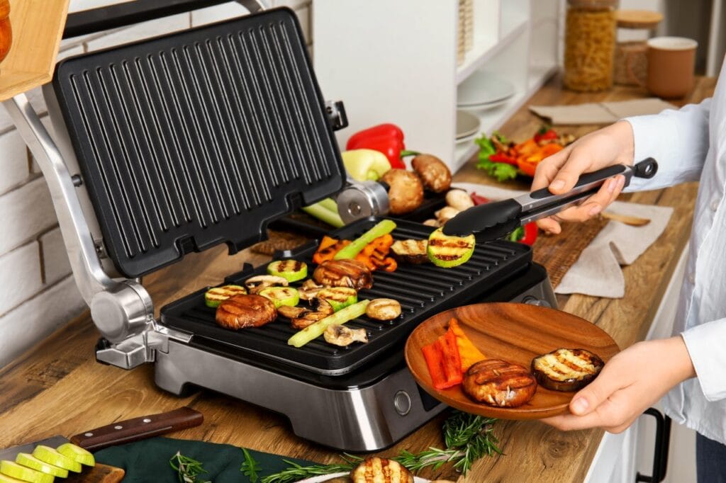 Grill electric deschis cu suprafețe din aluminiu turnat și legume la grătar pe plăci rezistente
