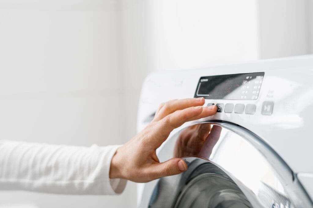 Persoană selectând programul unei mașini de spălat cu uscător modernă