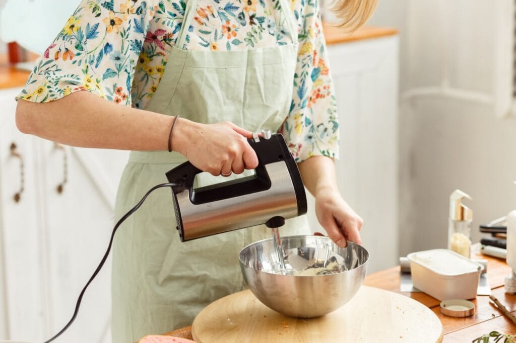 Mixerul tău merită un partener pe măsură: bolul corect Persoană care folosește un mixer electric într-un bol de inox pe blat de lemn, combinație optimă pentru stabilitate și eficiență