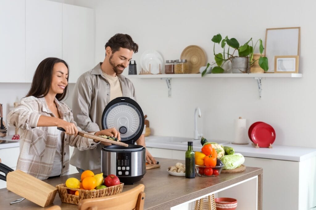 Tineri gătesc legume într-un multicooker modern într-o bucătărie albă, concept smart cooking pentru viață agitată