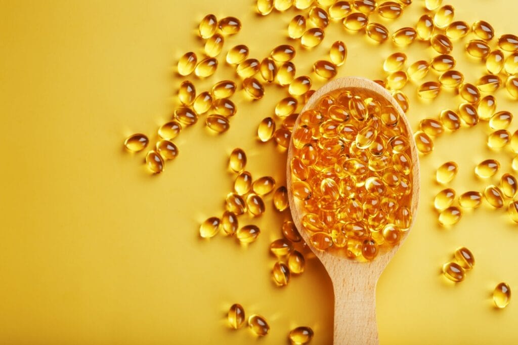 Când alimentația nu e suficientă, suplimentele cu D3 fac diferența Lingură de lemn plină cu capsule de vitamina D3, pe fundal galben, simbolizând suplimentarea nutrițională