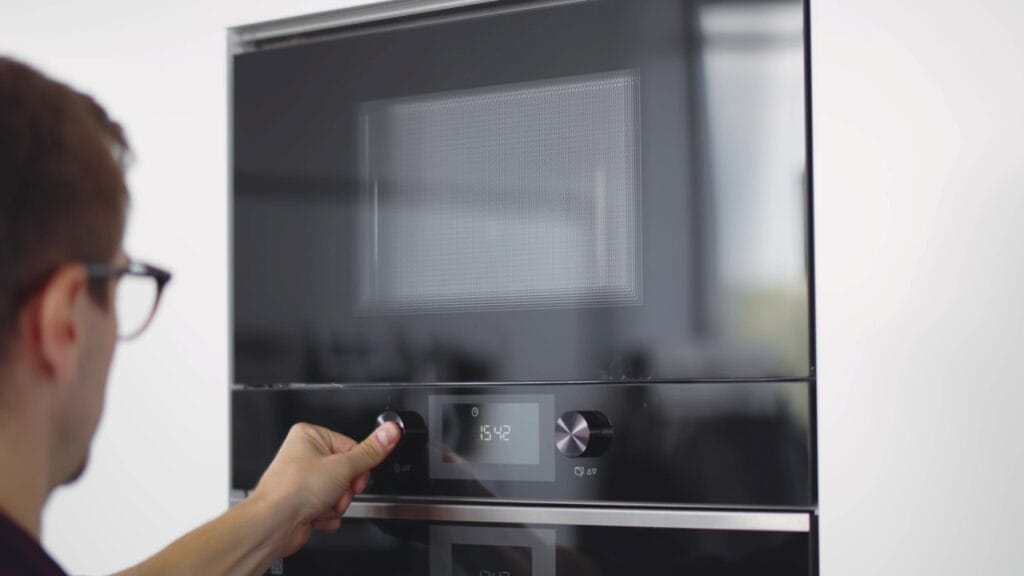 Persoană setând un cuptor cu microunde incorporabil negru cu display digital pentru eficiență energetică