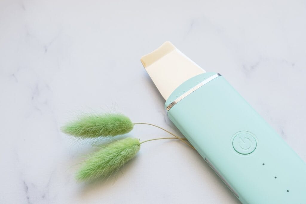 Dispozitiv de curățare ten compact, portabil și ușor, în nuanță verde mentă, pe fundal alb de marmură.