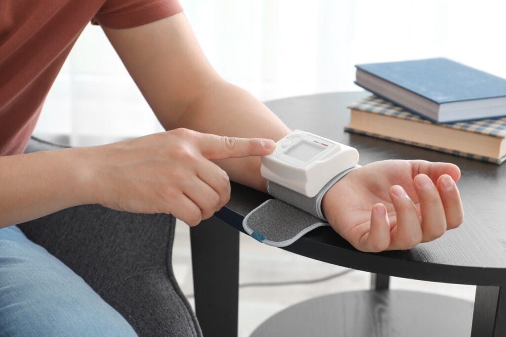 Cum să obții rezultate corecte la măsurarea tensiunii arteriale Persoană care își monitorizează tensiunea cu un tensiometru automat de încheietură, stând relaxată la masă.