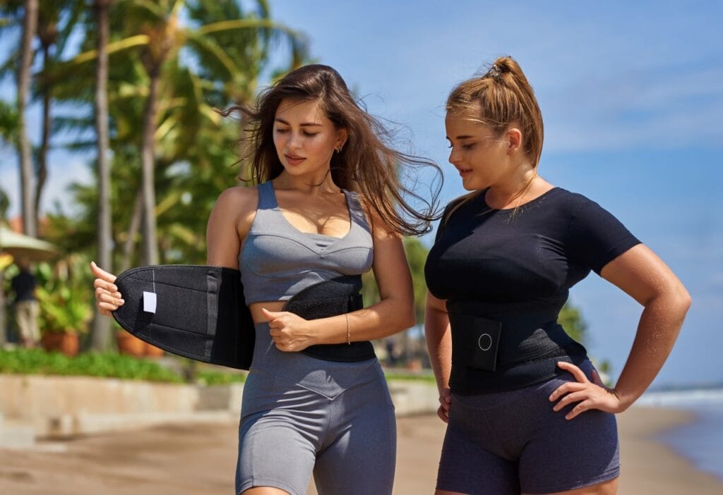 Neopren, latex sau lycra? Ghidul complet al materialelor pentru centuri de slăbit Două femei purtând centuri de slăbit din neopren și poliester pe plajă tropicală