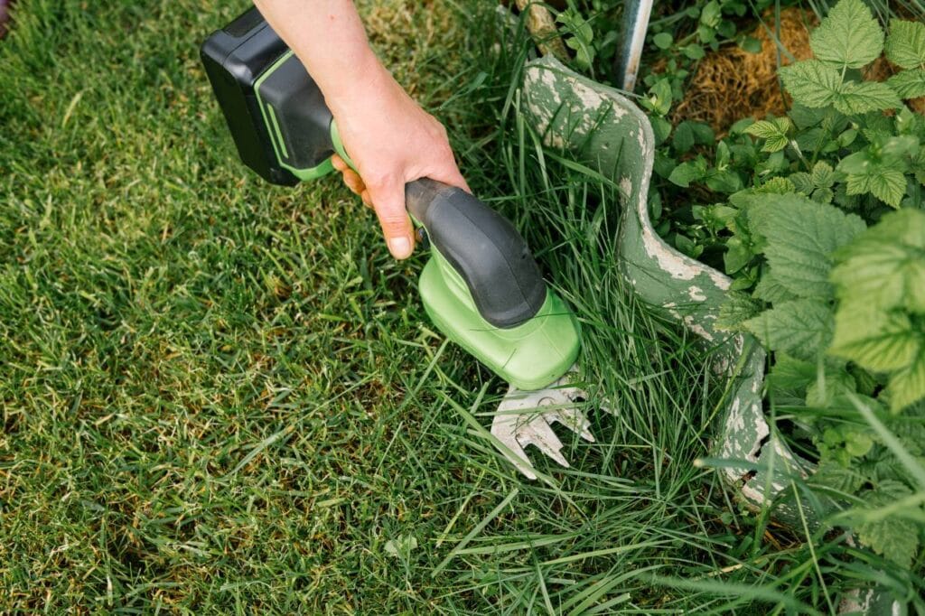 Grădinar folosind un foarfece electric 2-în-1 pentru margini de gazon și arbuști