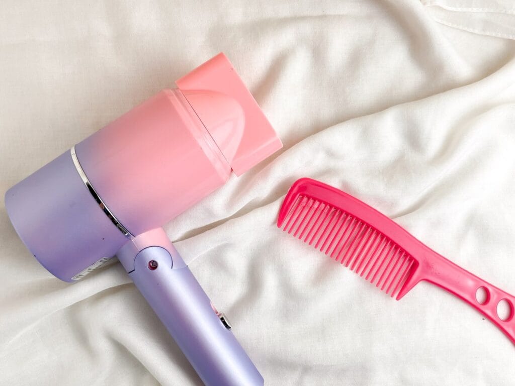 accesorii styling păr uscător colorat și pieptene roz pe fundal alb