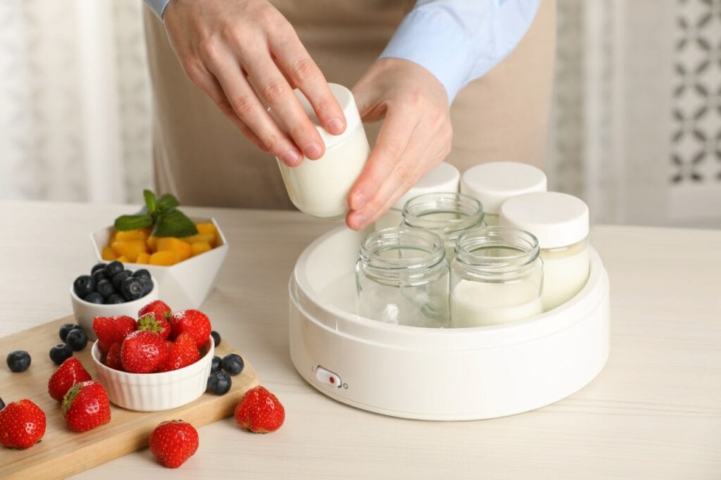 Persoană folosind yogurtieră pentru a prepara iaurt de casă, alături de fructe proaspete
