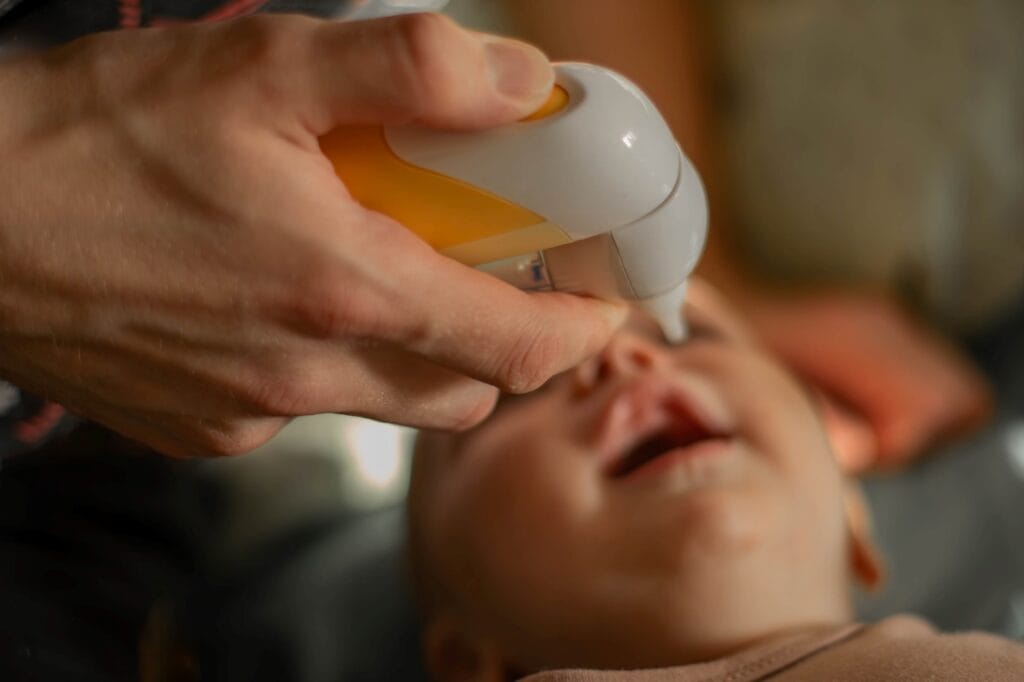 Părinte folosește aspirator nazal electric pentru a curăța nasul unui bebeluș răcit