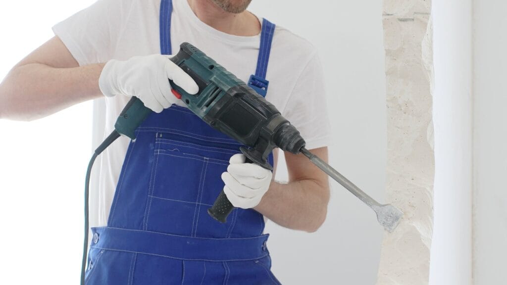 Muncitor folosind ciocan rotopercutor ergonomic cu mâner lateral cauciucat pentru spargere perete.