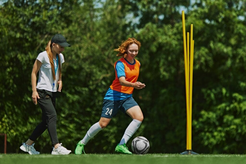 Antrenor și jucătoare la antrenament: tehnici pentru controlul mingii de fotbal Antrenor oferind sfaturi despre controlul mingii de fotbal pe teren la antrenament cu jucătoare