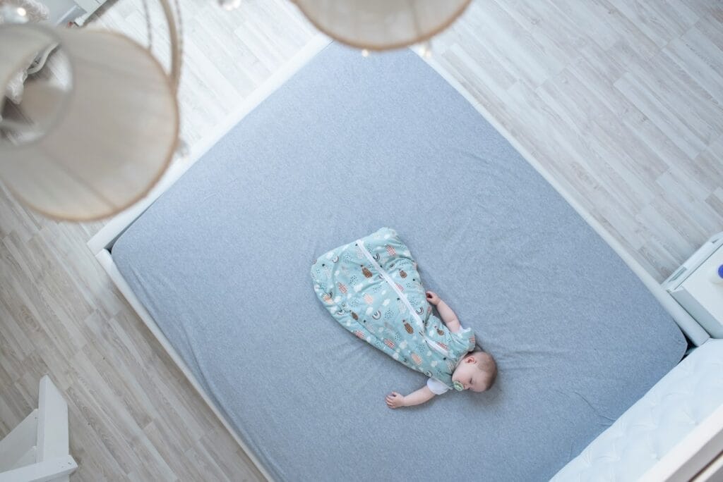 Bebeluș liniștit într-un sac de dormit modern pe pat bebeluș în sac de dormit pe pat mare, somn sigur și confortabil