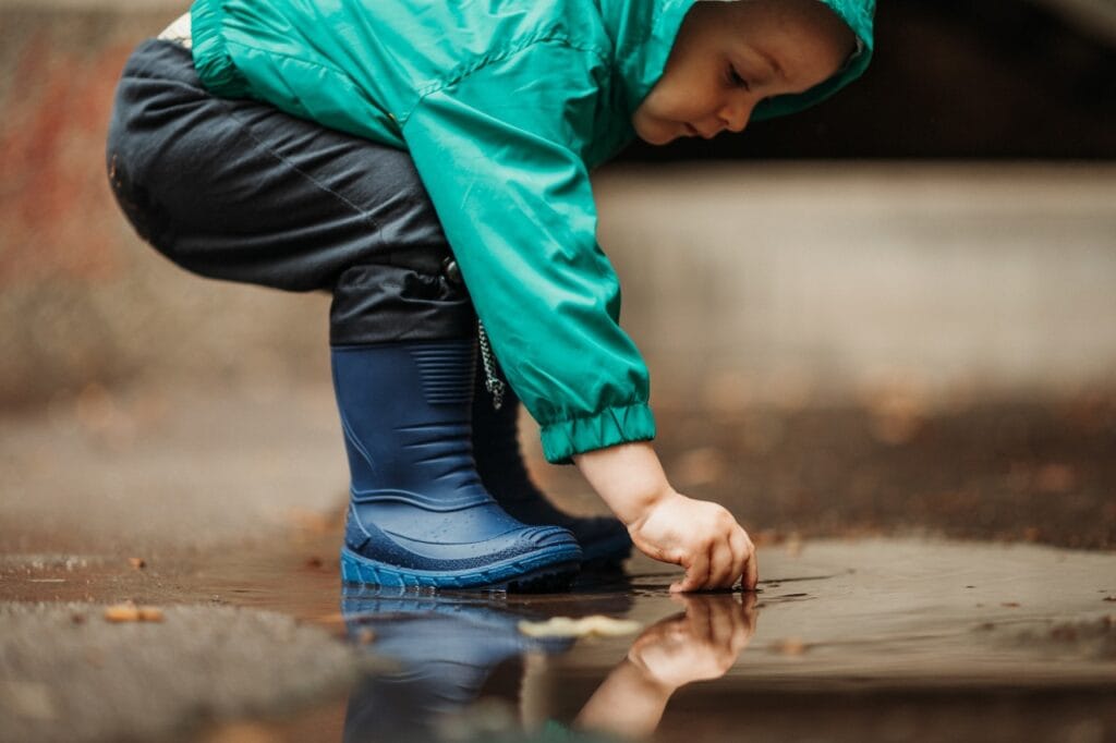 copil cu cizme de ploaie din material impermeabil sigur jucându-se în baltă