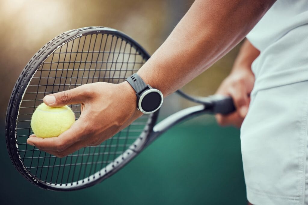 Verificare presiune minge de tenis, pregătire serviciu, mână cu ceas smart și rachetă, tenis outdoor.