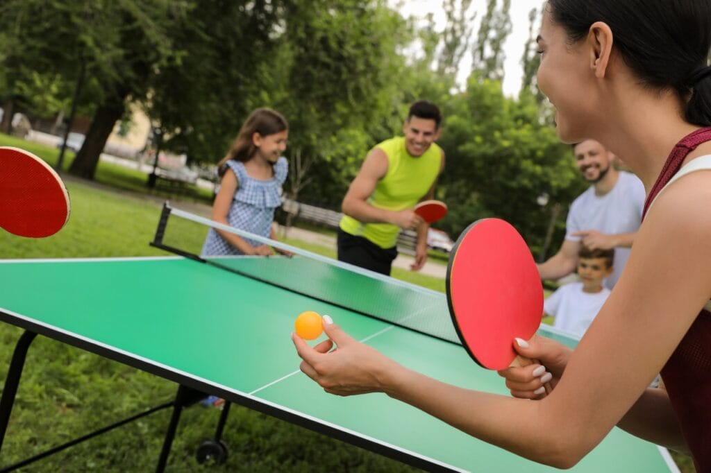 familie jucând ping-pong afară pe masă de tenis, activitate sportivă pentru toate vârstele