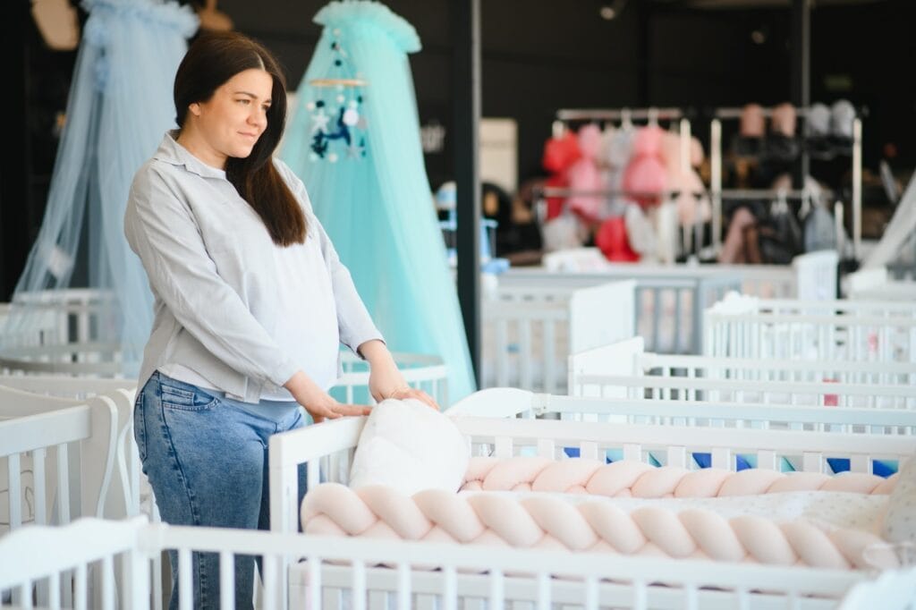 femeie însărcinată analizând pătuțuri din lemn și accesorii pentru bebeluși într-un magazin de profil