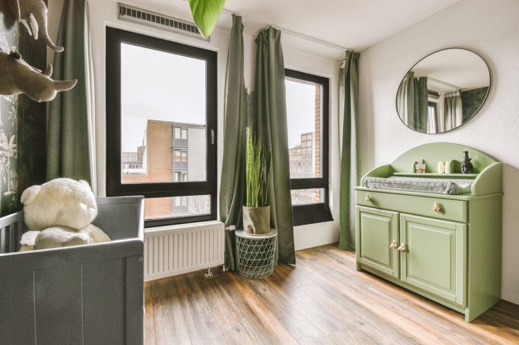 Comodă de înfășat verde, cu spații de depozitare și accesorii utile, plasată într-o cameră luminoasă pentru copii.