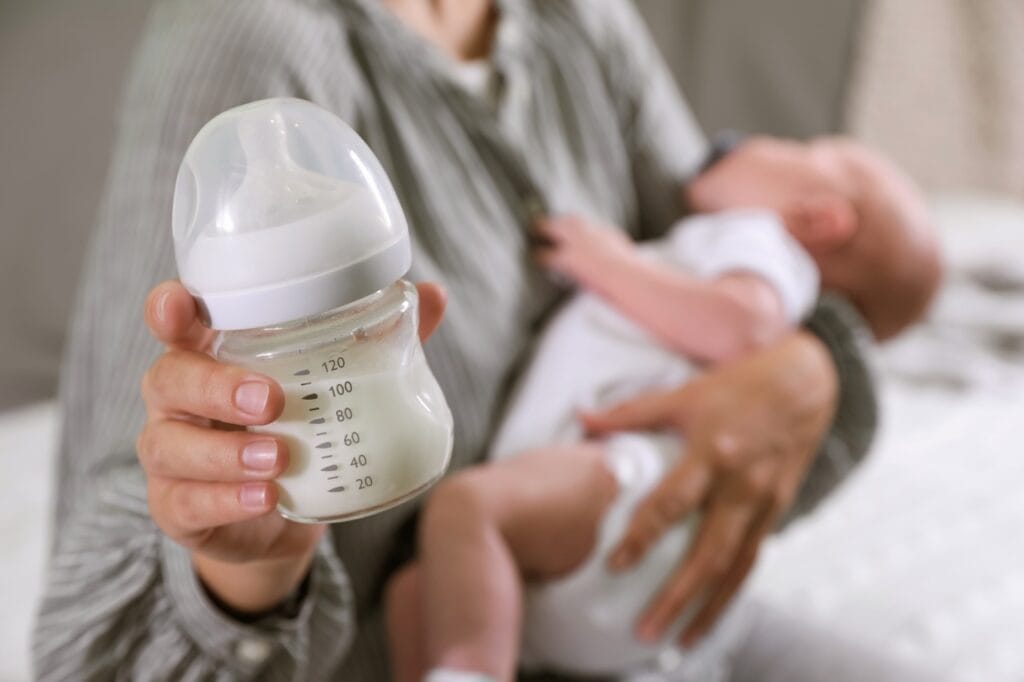 mamă ținând un bebeluș și un biberon, adaptare ușoară de la sân la biberon