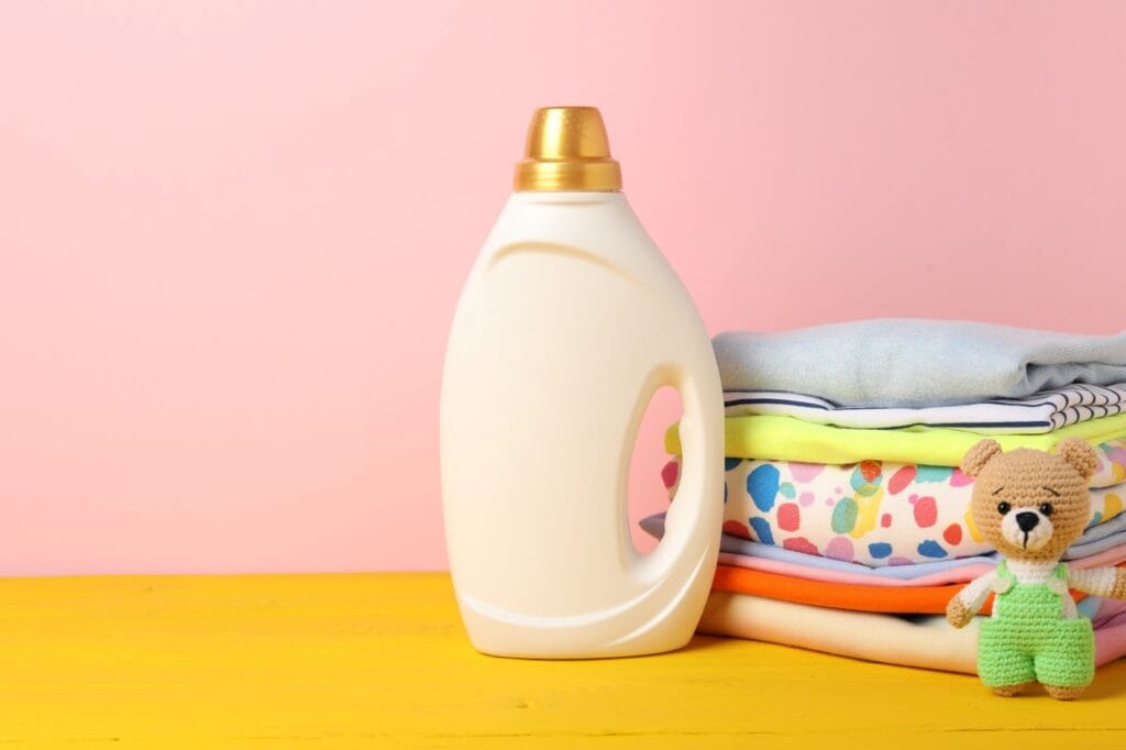 Balsam de rufe pentru copii, sticlă crem lângă haine colorate și ursuleț croșetat, rolul parfumului la balsamuri pentru hainele copiilor