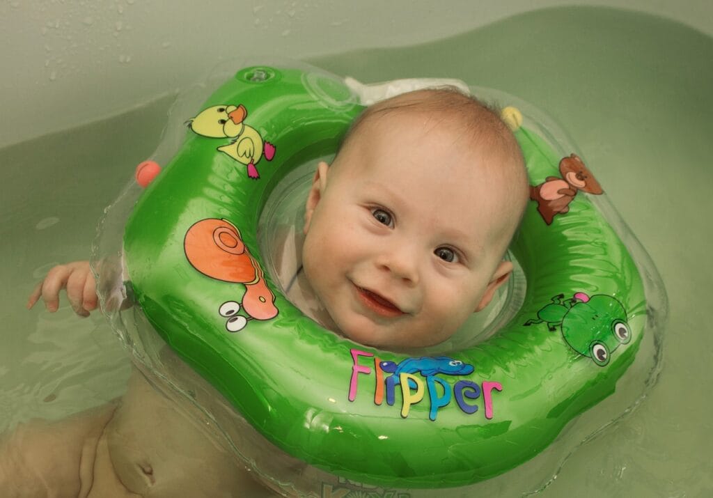 bebeluș fericit în cadă cu colac de gât verde, recomandat de pediatri și kinetoterapeuți