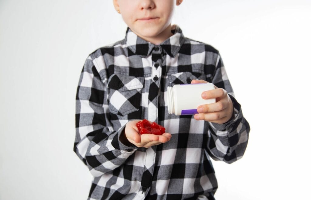 Vitamine pentru imunitatea copiilor: cum arată o administrare corectă Copil care ține jeleuri cu vitamine pentru imunitate și ia suplimente într-un mod ușor de administrat