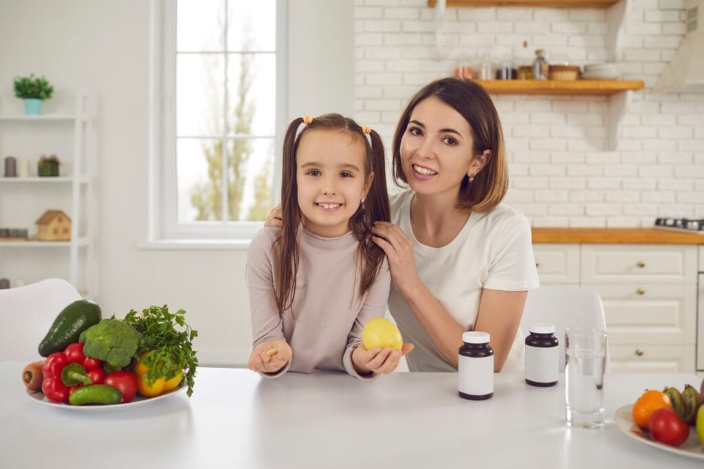 Vitamina C pentru copii: naturală sau de sinteză? Mamă și fiică alegând între fructe proaspete și suplimente cu vitamina C pentru copii, în bucătărie