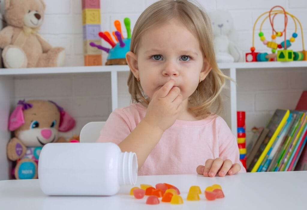 De ce contează doza corectă de vitamina C la copii? Fetiță mică gustând jeleuri de vitamina C, concept despre dozajul potrivit la copii